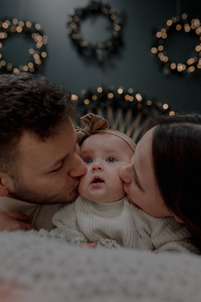 Parents lovingly kiss their baby indoors, capturing a cozy winter family moment.
