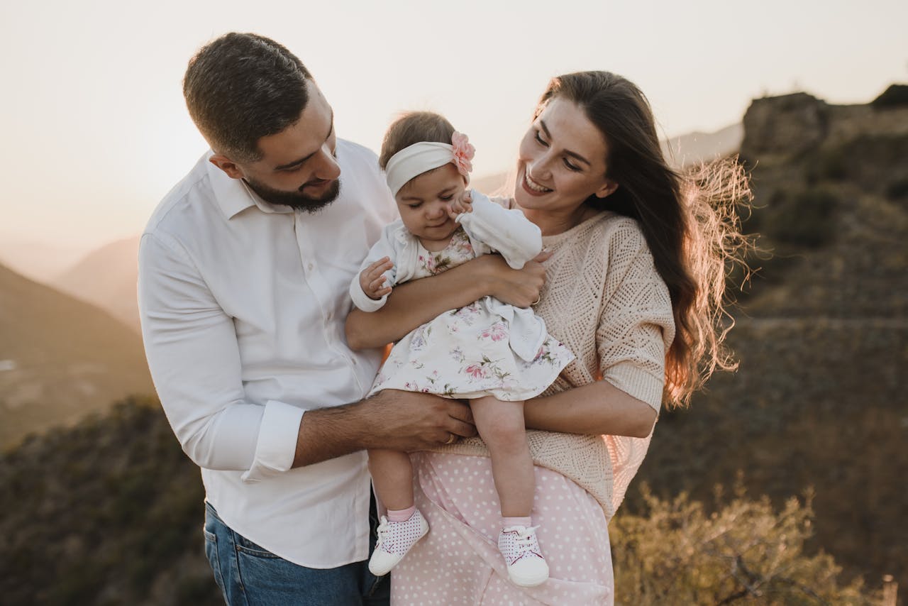 A joyful family moment with parents and baby outdoors during sunset, capturing warmth and happiness.